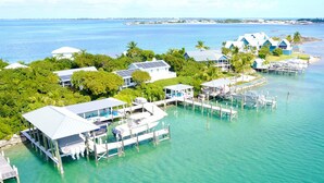 An aerial view of a coastal resort with multiple overwater bungalows connected by walkways, clear turquoise waters, and lush greenery. - Luxury oceanfront villa 1BR, protected dock, private & gated peninsula (Marsh Harbour)