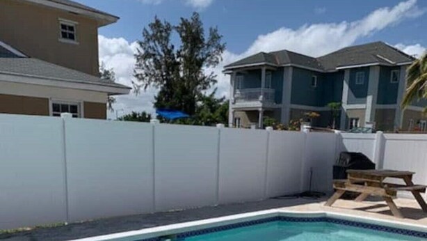 A rectangular swimming pool with clear blue water, surrounded by a white fence and a wooden picnic table. - Entire Guest Suite - 1 bedroom (Nassau)