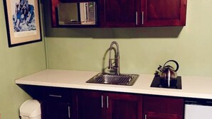 A compact kitchen with dark wooden cabinets, a white countertop, a stainless steel sink, and a kettle. - Entire Guest Suite - 1 bedroom (Nassau)