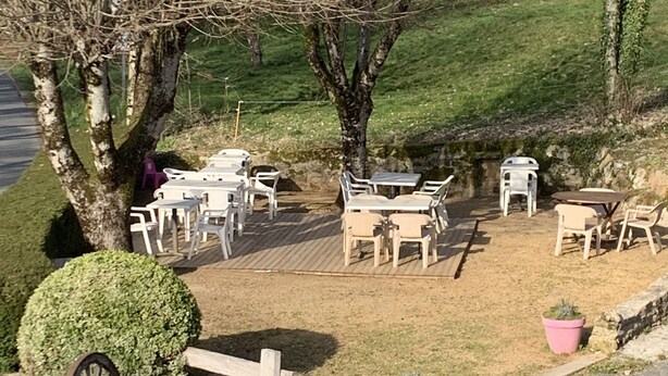 An outdoor seating area with tables and chairs, surrounded by trees and a stone wall. - Domaine Le Colombié  (Gorses)