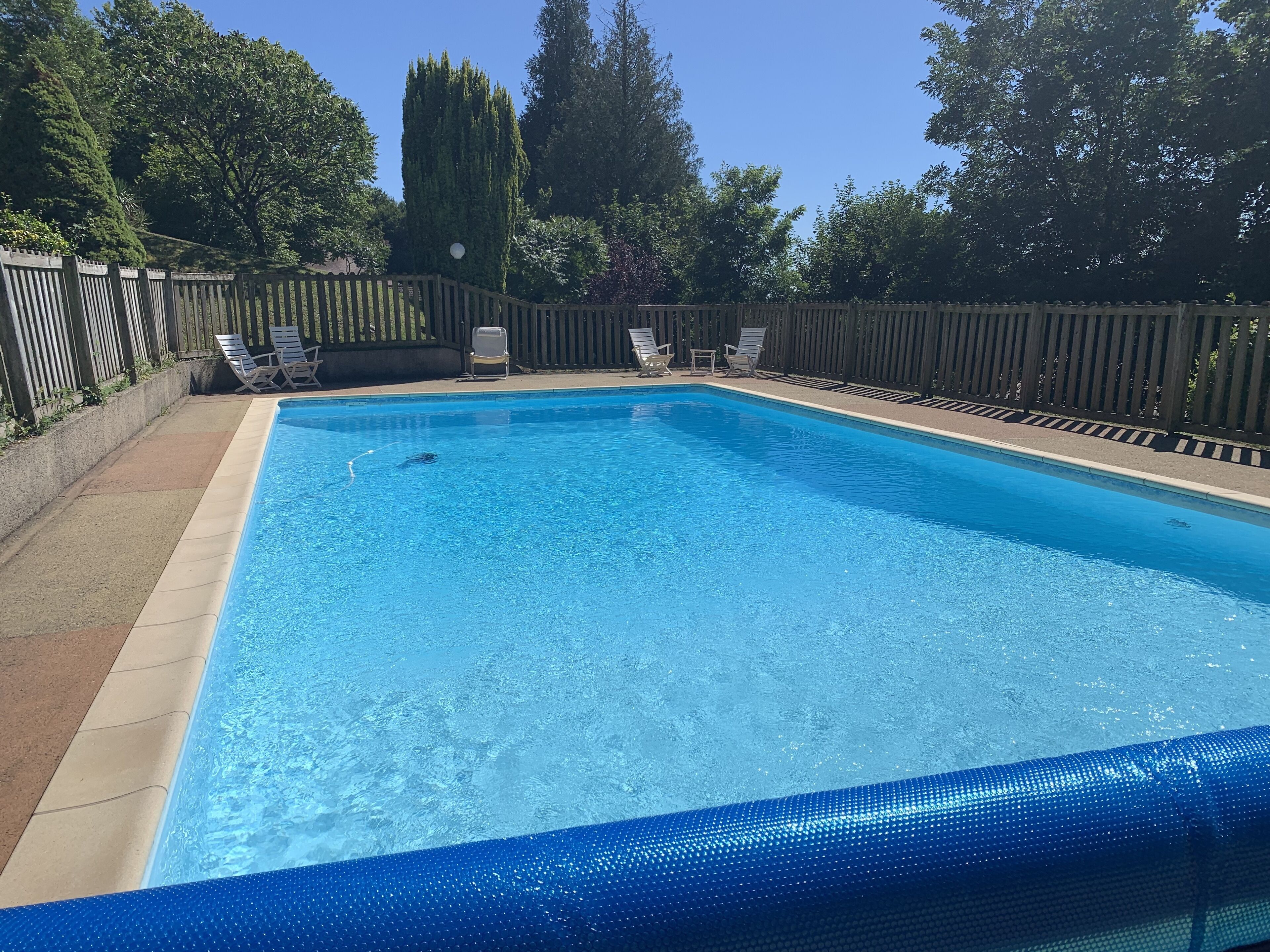 Une piscine rectangulaire à bordure bleue, entourée d’une clôture en bois et d’une terrasse en béton.