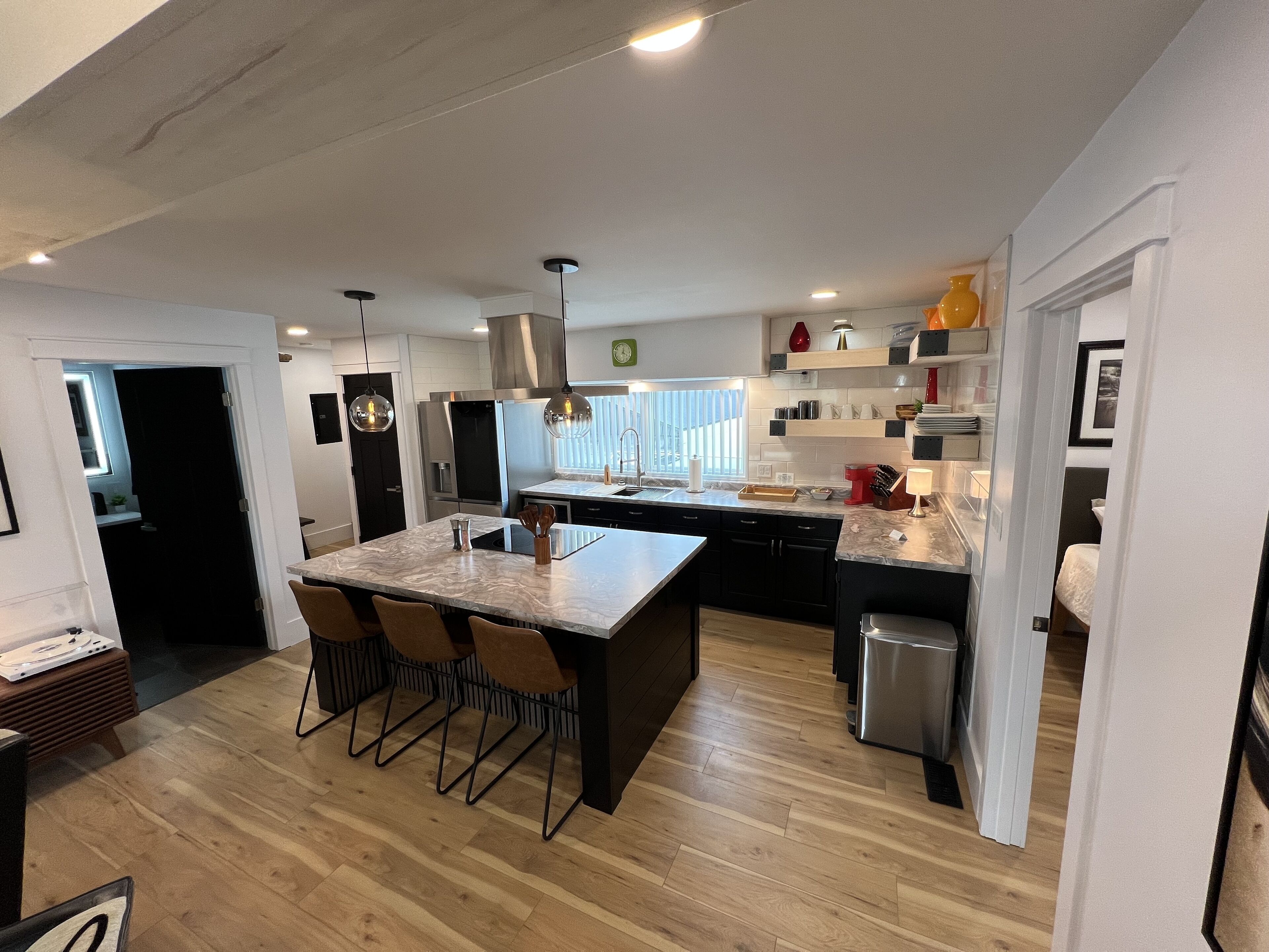 Een moderne keuken met een centraal eiland, zwarte kasten, roestvrijstalen apparatuur en houten vloeren.