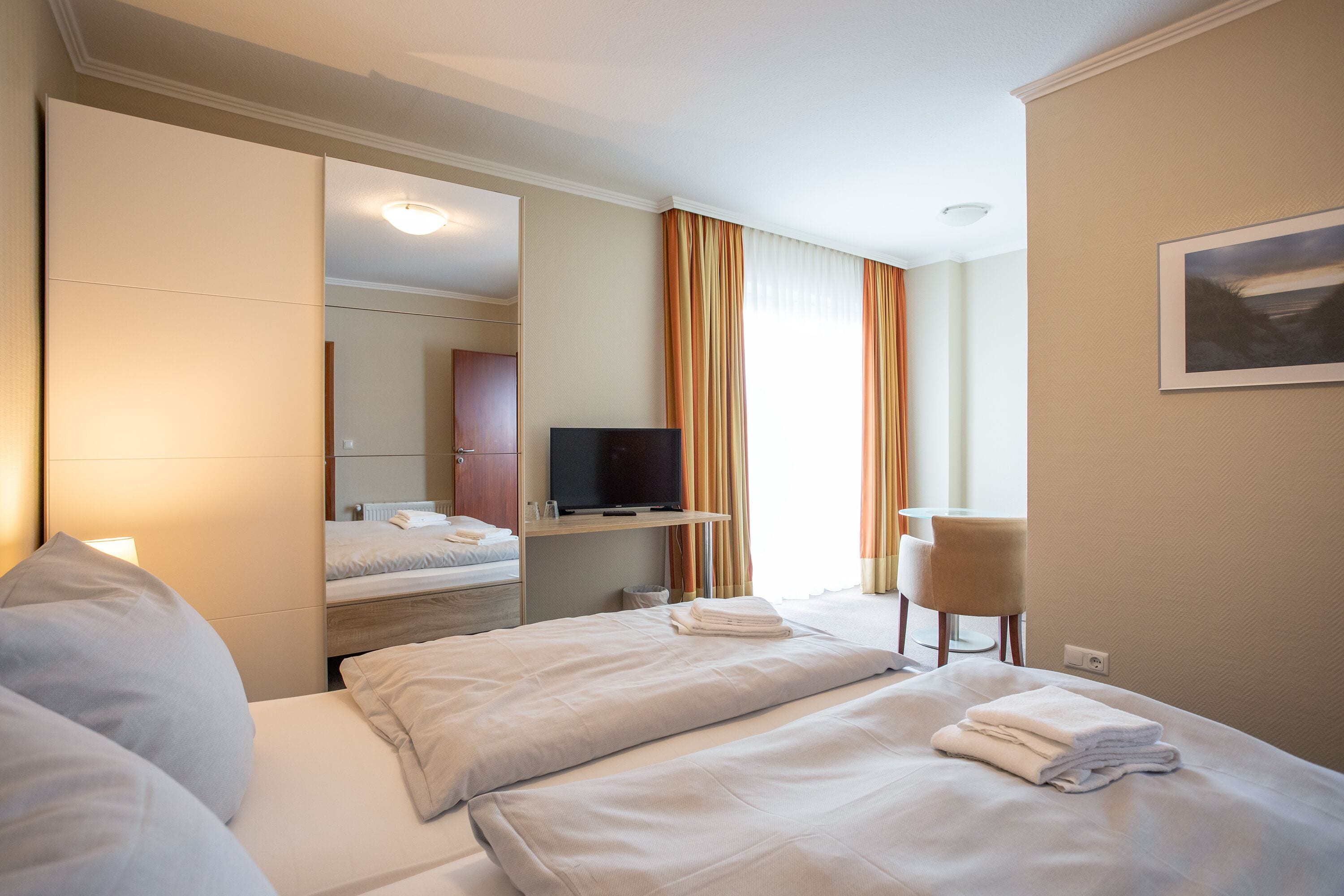 Hotellihuone, jossa on kaksi sänkyä, televisio, tuoli ja suuri ikkuna, jossa on verhot.