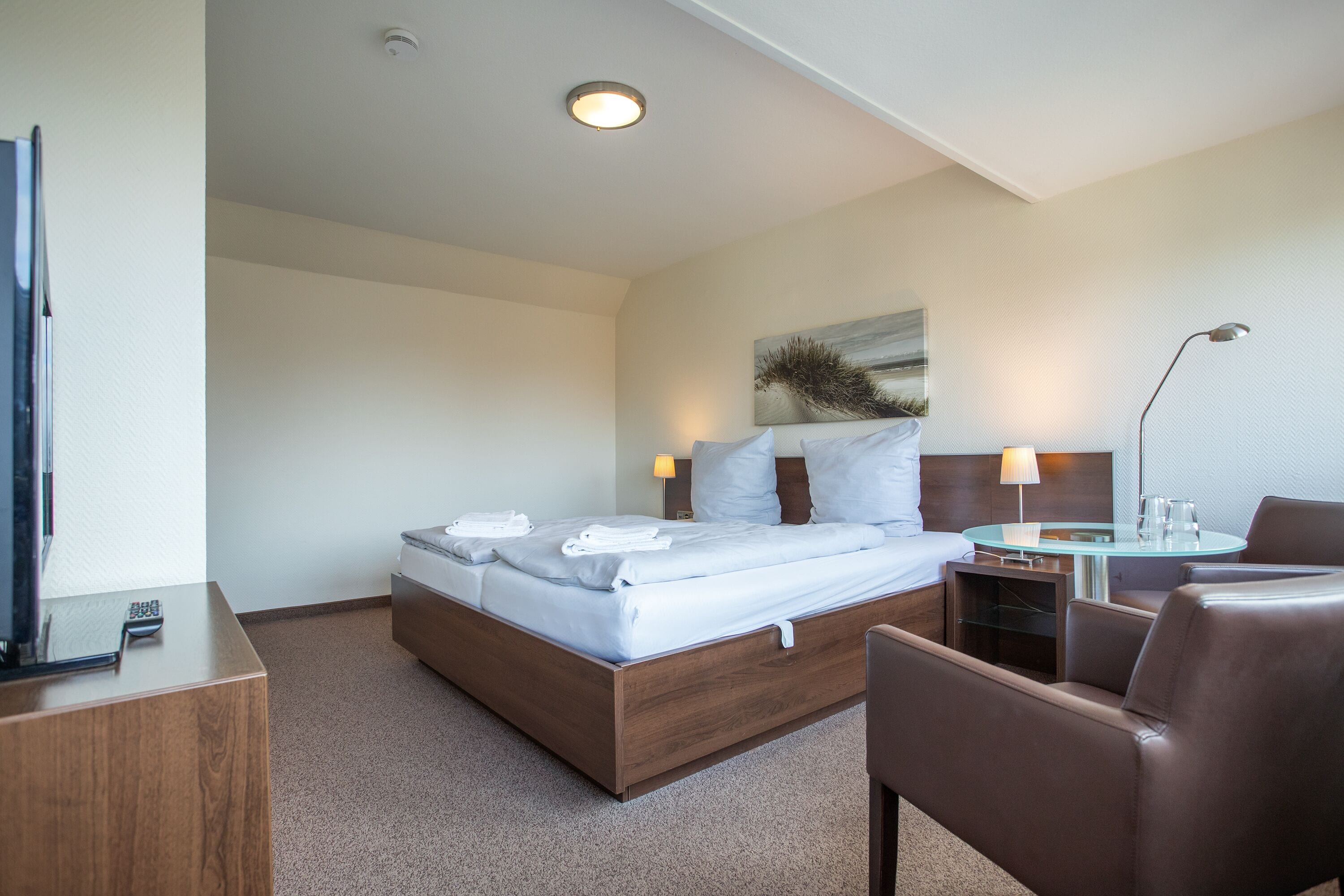 Une chambre d’hôtel avec un lit, un bureau, une chaise, une lampe et un tableau au mur.