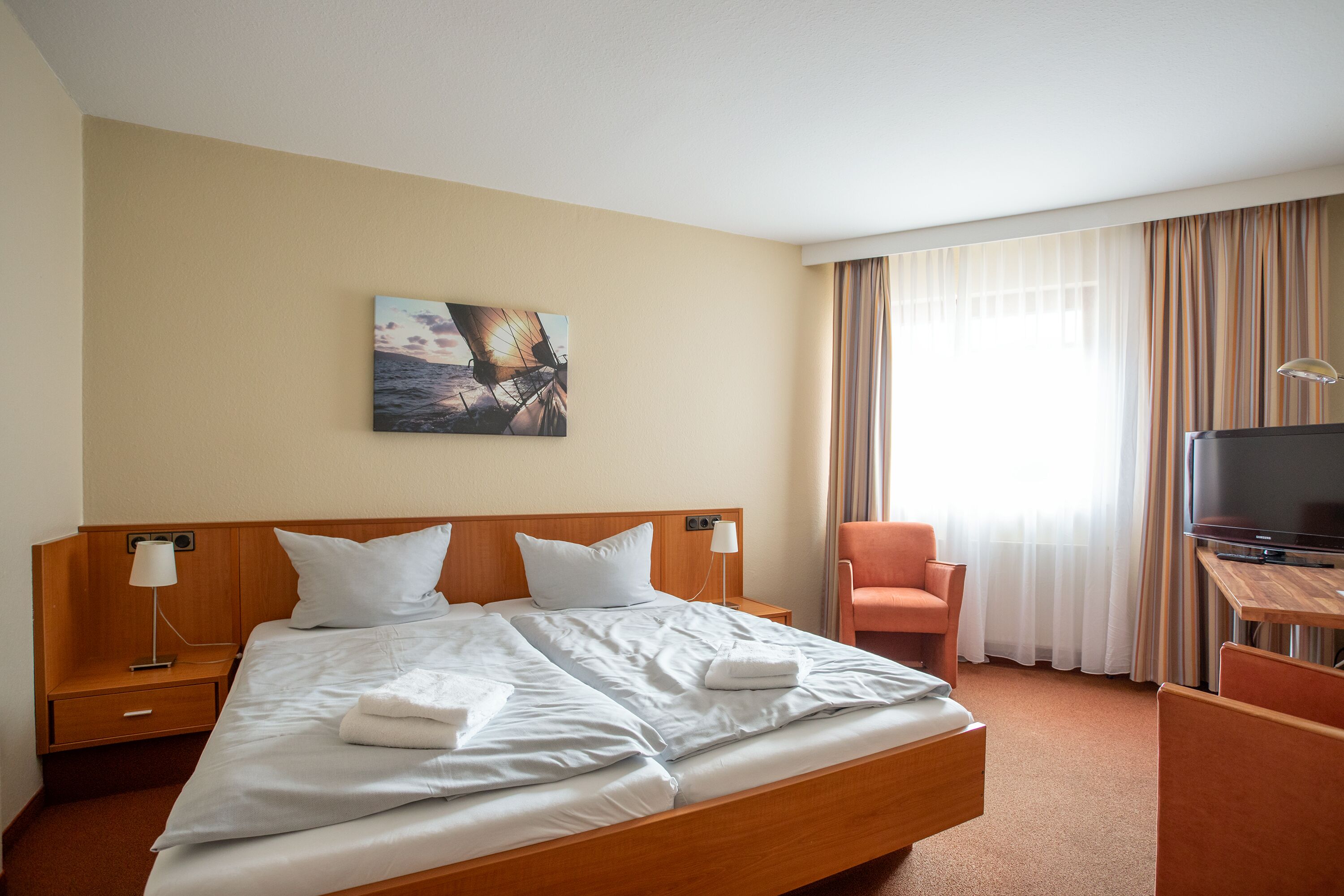 Une chambre d’hôtel avec un grand lit, un bureau avec une télévision, une chaise et un tableau au mur.