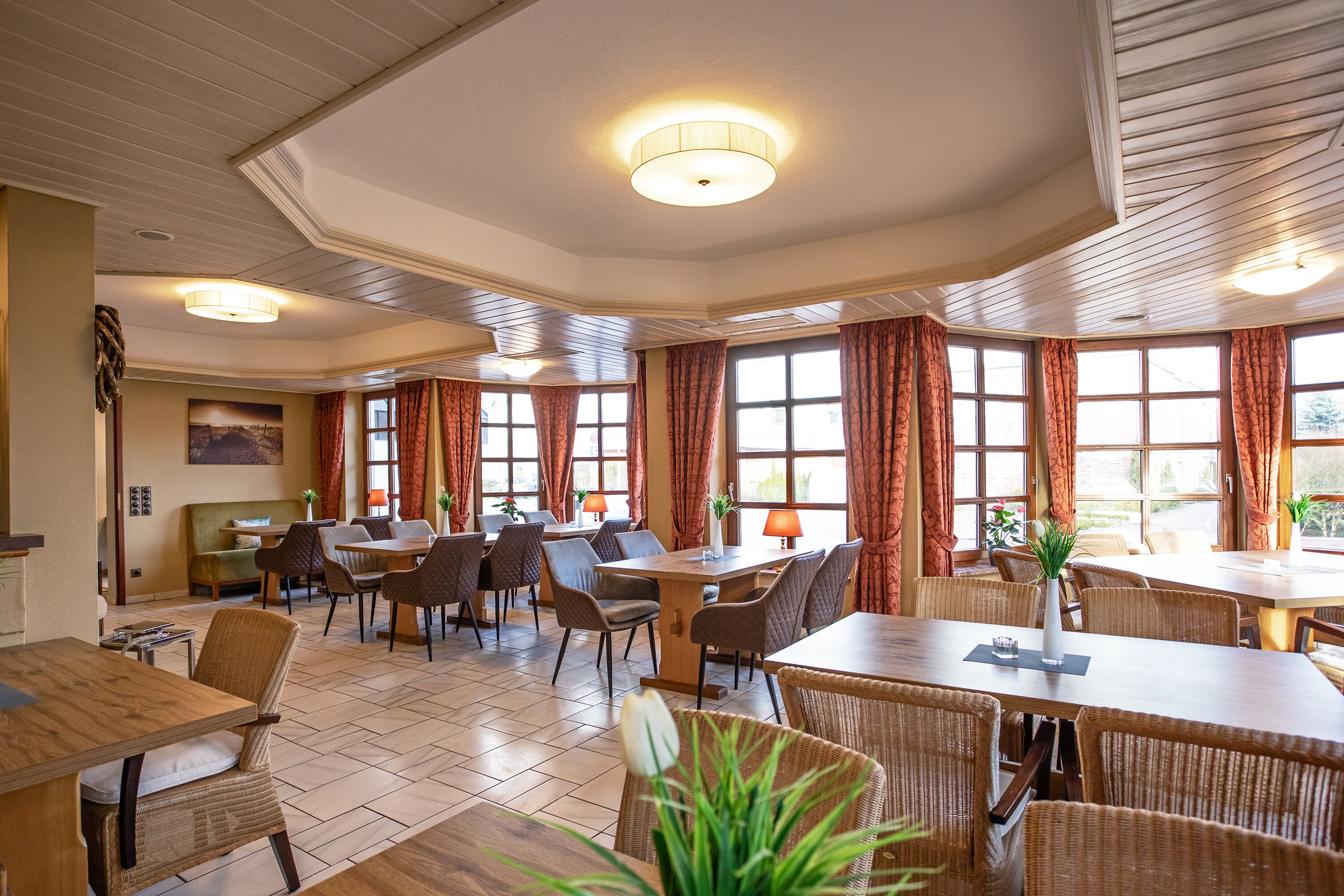 Un'ampia sala da pranzo con diversi tavoli e sedie, grandi finestre con tende e un soffitto con illuminazione a incasso.