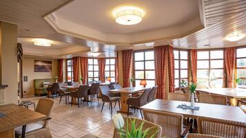 Un'ampia sala da pranzo con diversi tavoli e sedie, grandi finestre con tende e un soffitto con illuminazione a incasso.