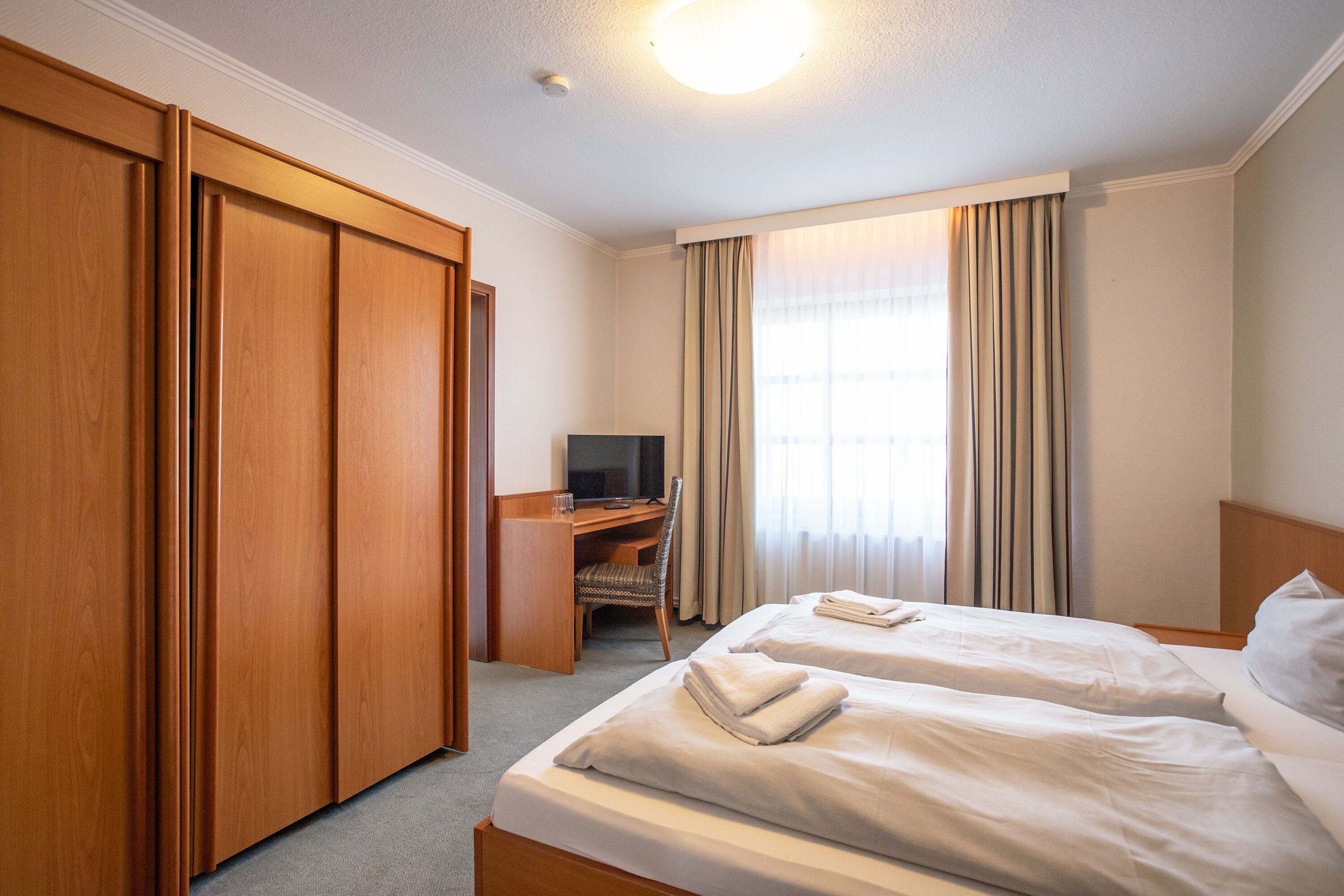 A hotel room with two beds, a desk, a TV, and a wardrobe.