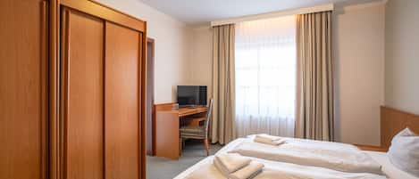 A hotel room with two beds, a desk, a TV, and a wardrobe.