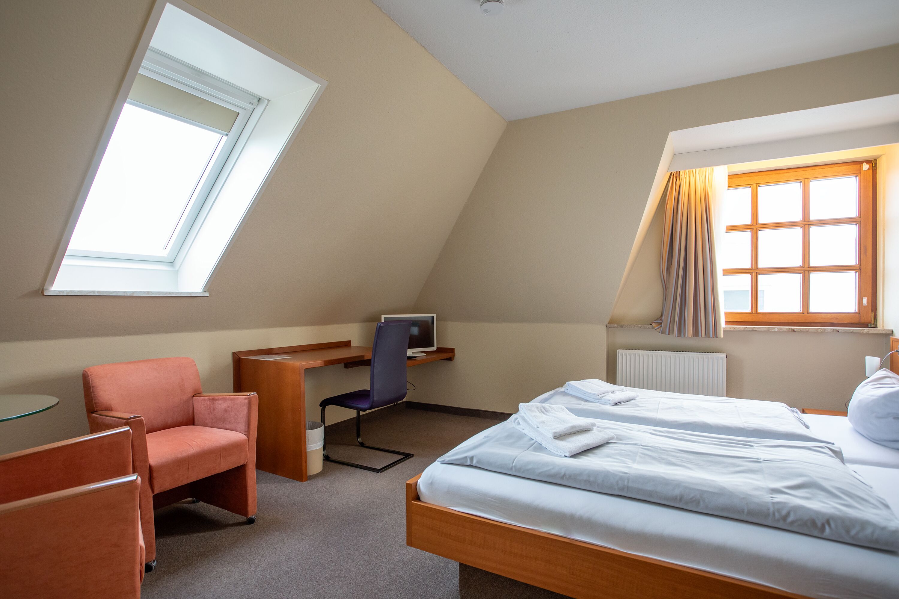 A bedroom with a bed, a desk, a chair, and a window.