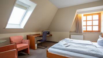 A bedroom with a bed, a desk, a chair, and a window.