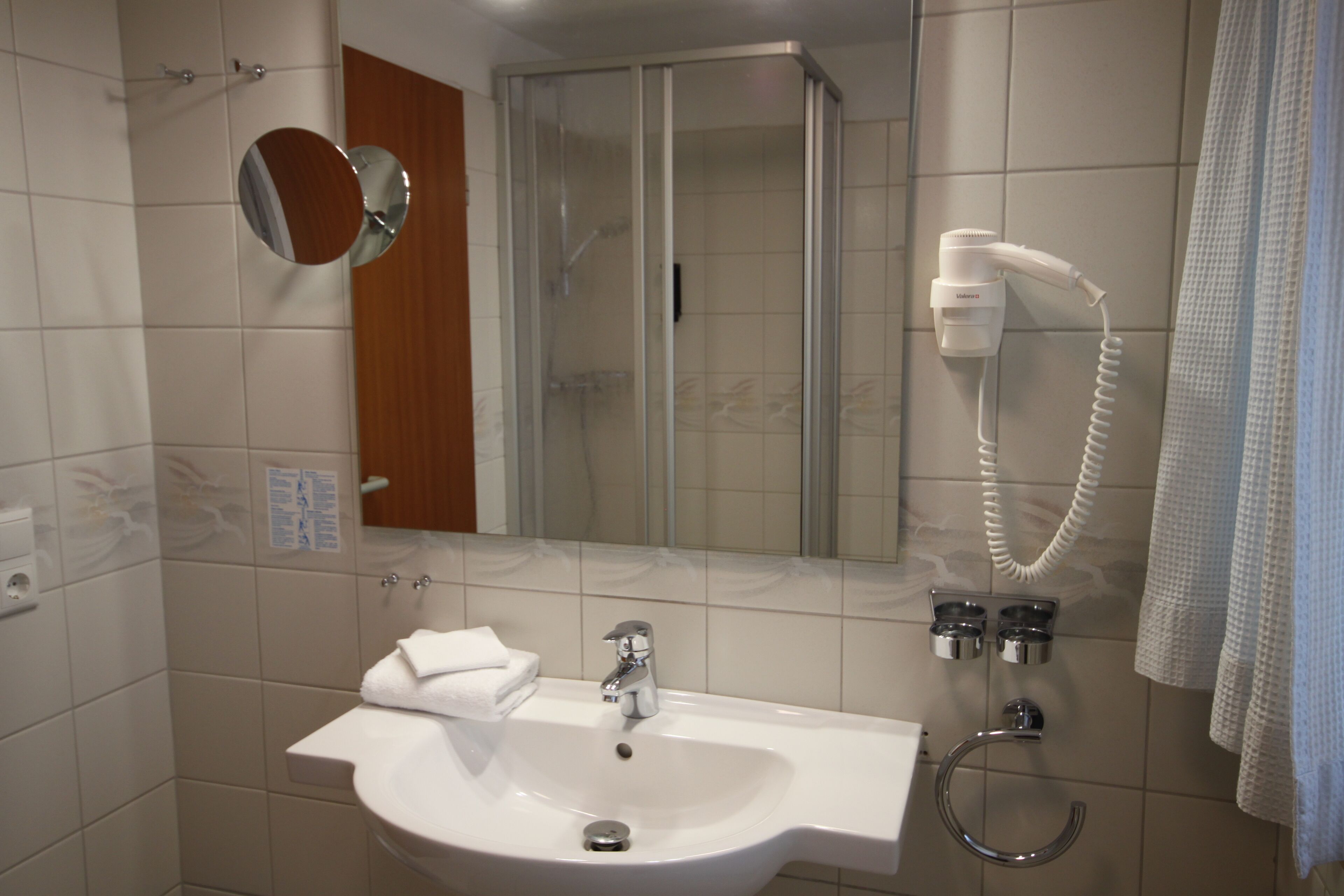 Un baño con lavabo, espejo y secador de pelo fijado a la pared.