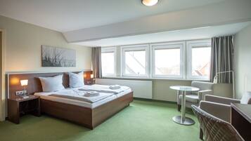 Une chambre d’hôtel comprenant un lit, des tables de chevet, un bureau, une chaise et une fenêtre avec des rideaux.