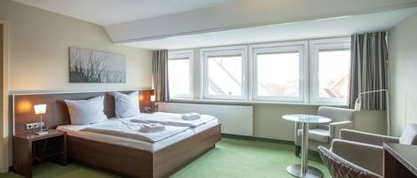 A hotel room with a bed, bedside tables, a desk, a chair, and a window with curtains.