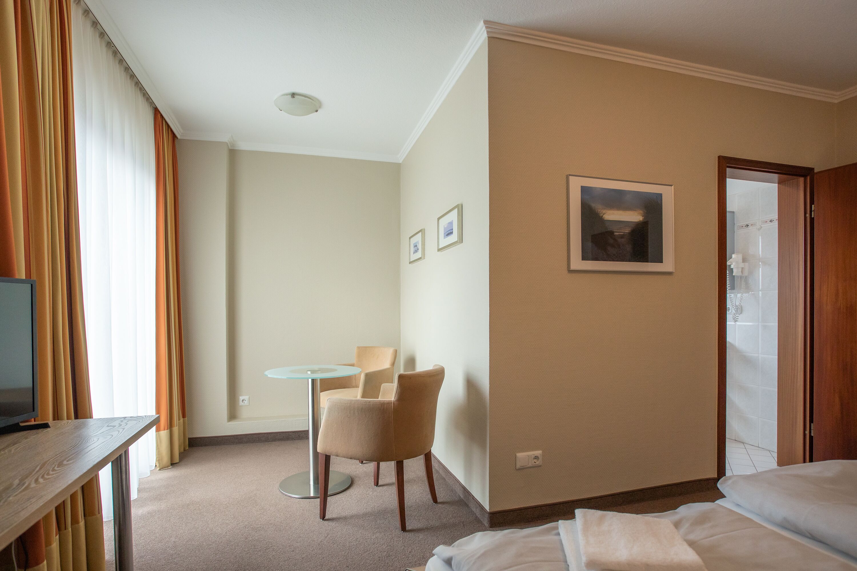 Ein Hotelzimmer mit Bett, Schreibtisch mit Fernseher, Stuhl, kleinem Tisch und einem Bild an der Wand.