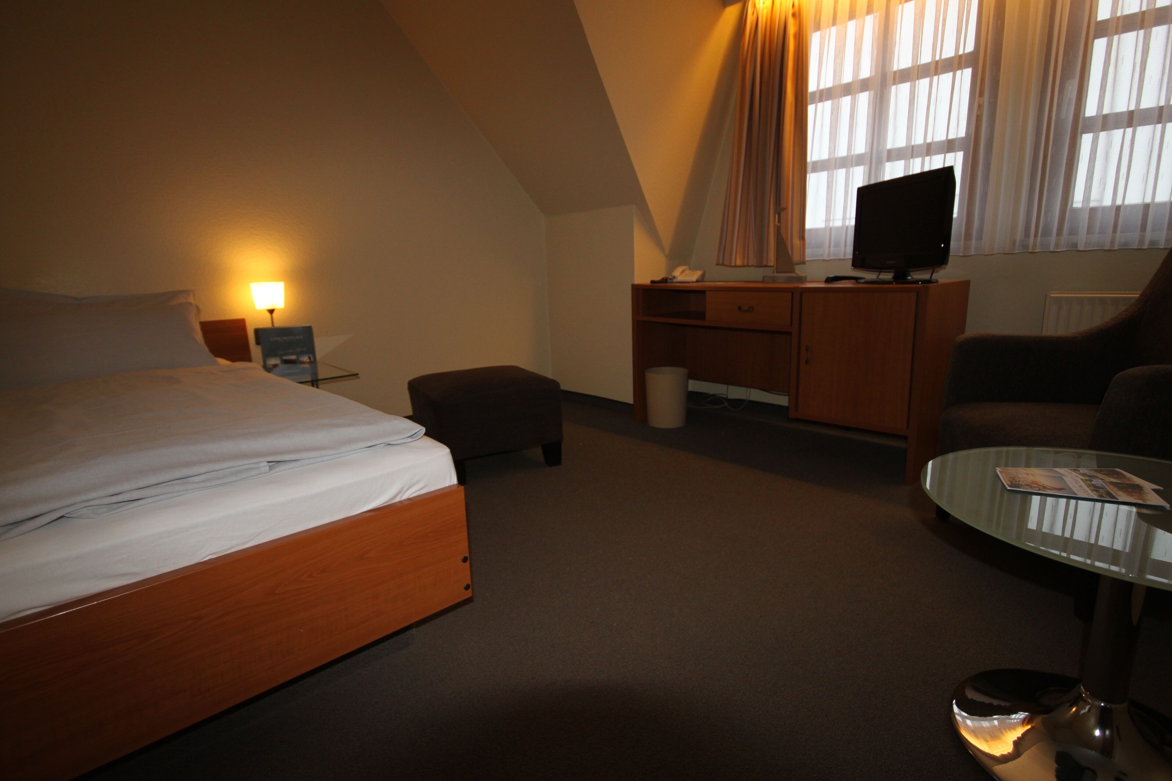 A hotel room with a bed, a desk with a computer, a chair, and a glass coffee table.