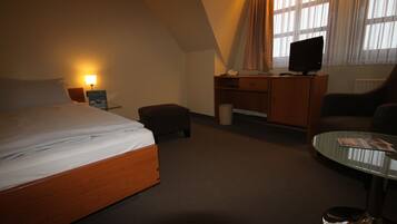 Une chambre d’hôtel comprenant un lit, un bureau avec un ordinateur, une chaise et une table basse en verre.