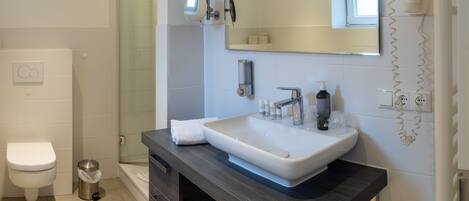 Un baño moderno con un lavamanos grande de color blanco, tocador de madera oscura, cabina de ducha de vidrio y un espejo con luz integrada arriba.