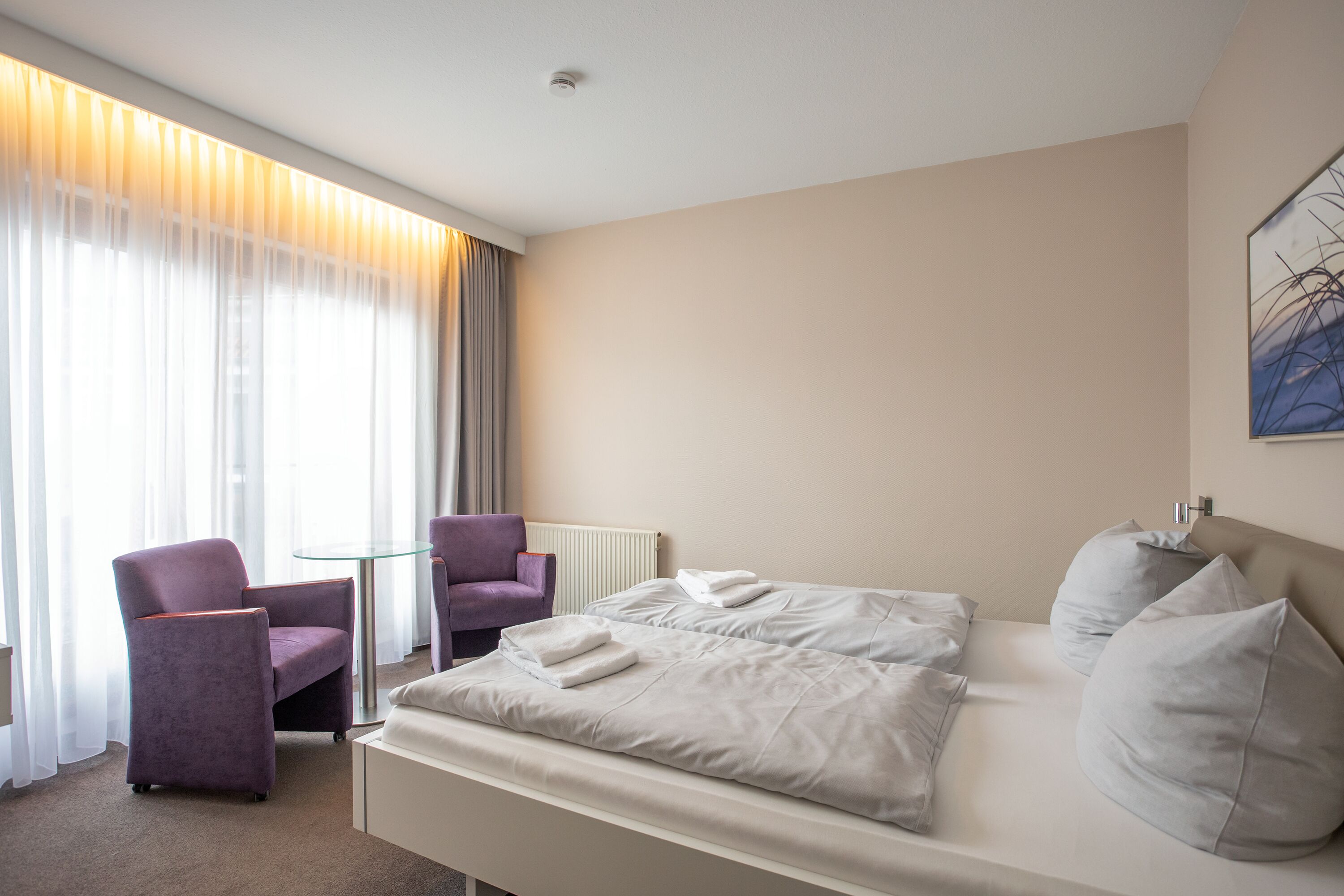 Una habitación de hotel con una cama, dos sillas, una mesita y una ventana con cortinas.