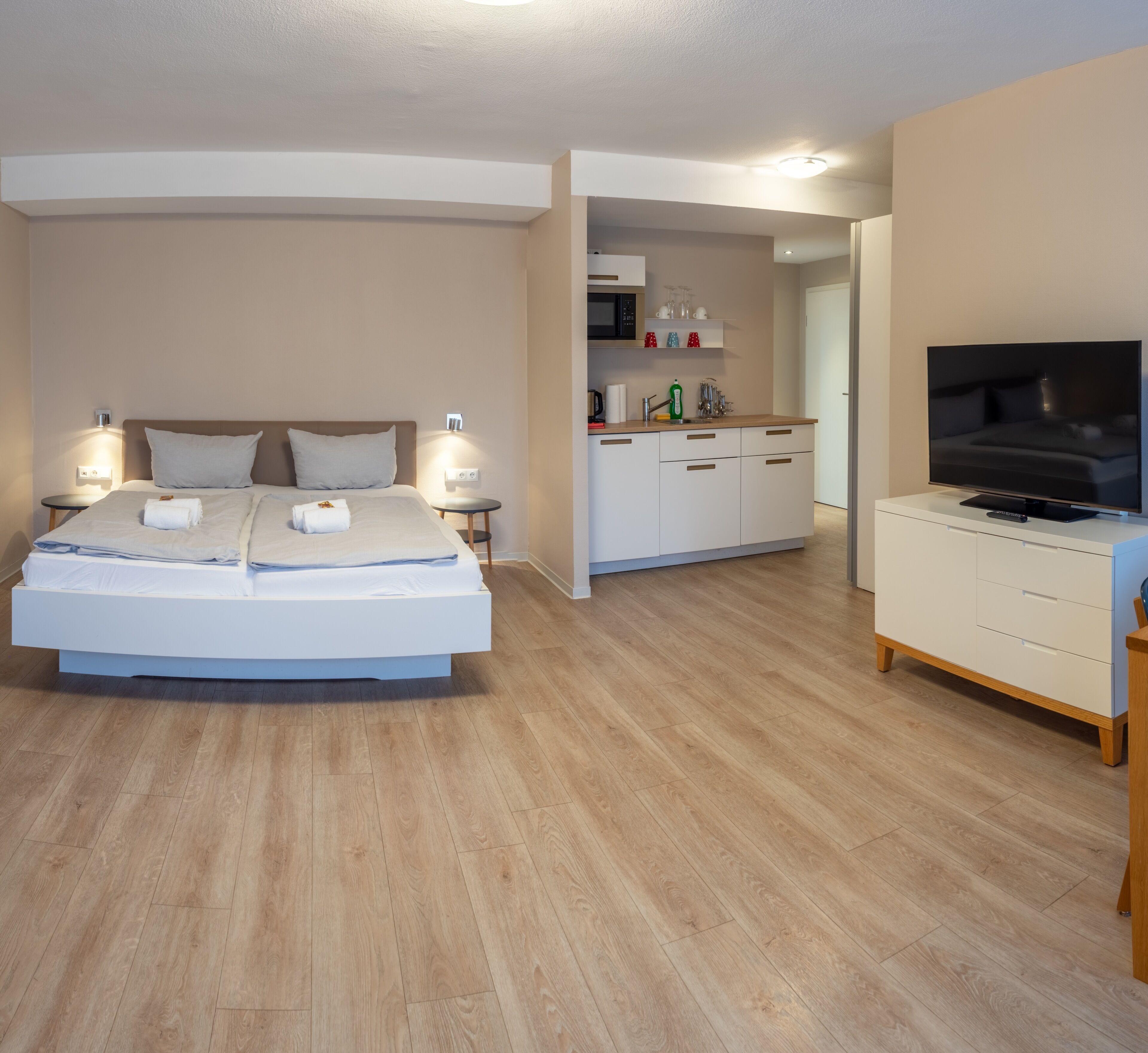 Een moderne hotelkamer met een groot bed, nachtkastjes, een flatscreen televisie, een kitchenette en een eethoek.