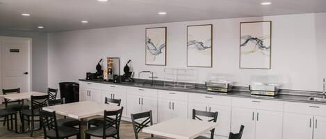 A modern kitchen with white cabinets, a black countertop, and three framed abstract paintings.