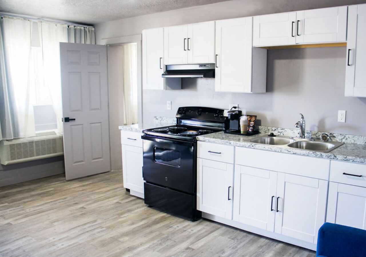 A compact kitchen with white cabinets, a black stove, and a sink.
