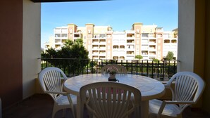A balcony with a round table and four chairs, overlooking a row of multi-story buildings with balconies. - Los Cisnes 77 - Two Bedroom Apartment, Sleeps 5 (Punta del moral)
