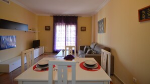 A dining area with a table set for two, a sofa, and a television in the background. - Los Cisnes 77 - Two Bedroom Apartment, Sleeps 5 (Punta del moral)