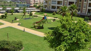 A playground with swings and slides, surrounded by well-maintained grass and palm trees. - Los Cisnes 77 - Two Bedroom Apartment, Sleeps 5 (Punta del moral)