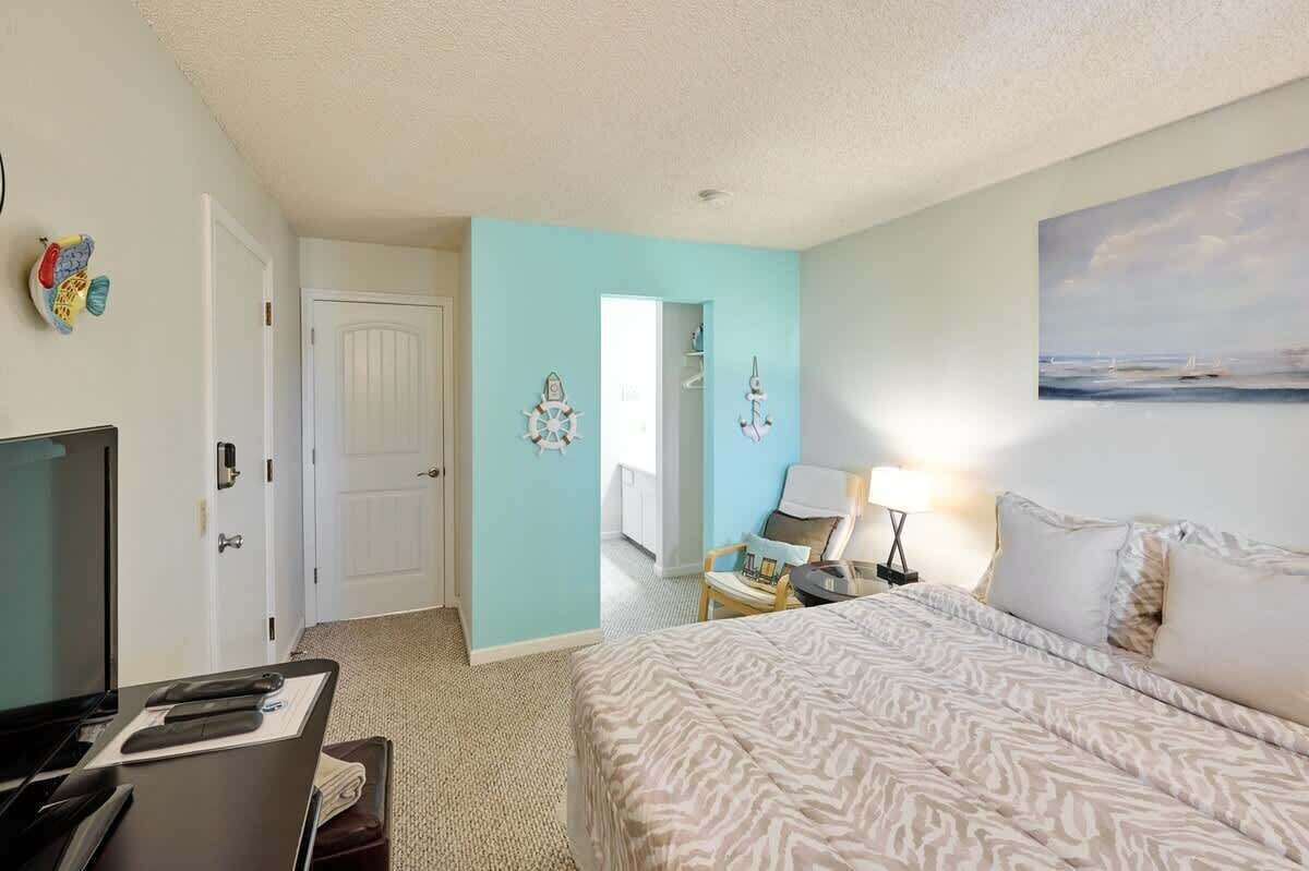 A hotel room with a bed, a desk, a chair, a TV, and a painting on the wall.
