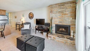 A living room with a stone fireplace, a television, and a dining area with a table and chairs. - Cute Ocean View Condo - Top Floor - Fireplace! (Lincoln City)