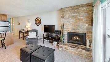 A living room with a stone fireplace, a television, and a dining area with a table and chairs.