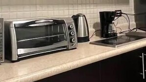 A kitchen with dark cabinets, a toaster oven, a coffee maker, and a tiled backsplash. - Departamentos FVD (Cabo San Lucas)