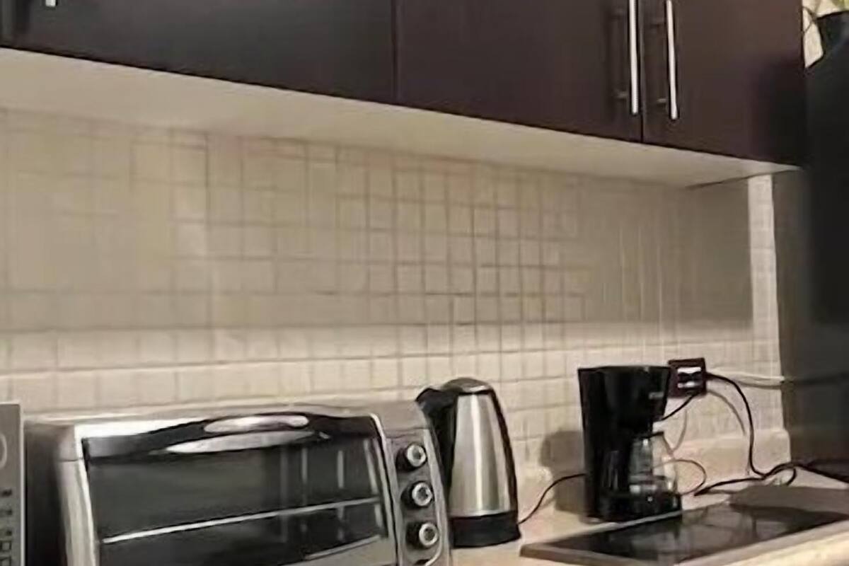 A kitchen with dark cabinets, a toaster oven, a coffee maker, and a tiled backsplash.