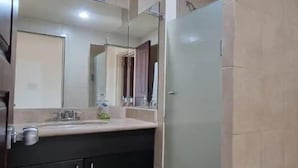 A bathroom with a glass shower enclosure, a sink with a mirror, and a dark-colored cabinet. - Departamentos FVD (Cabo San Lucas)
