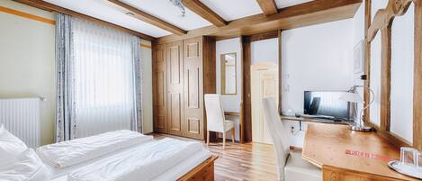 Habitación de hotel con cama de madera, un escritorio con silla, televisor y ventana con cortinas.