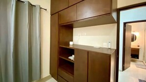 Una habitación con un armario de madera, un estante blanco y una puerta que da a otra estancia.