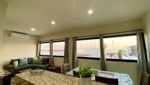 Una sala de estar con un sofá, una mesa de comedor y vistas al exterior a través de amplios ventanales.