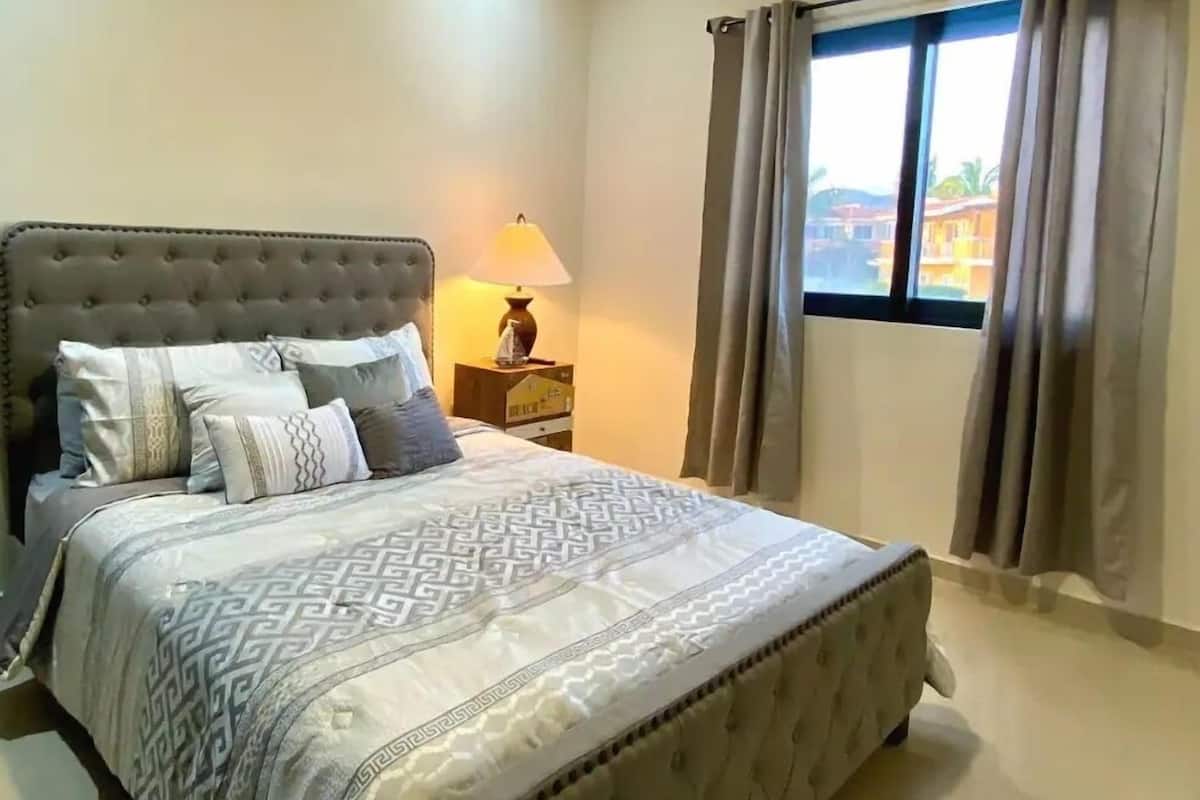 A neatly made bed with a patterned bedspread, a tufted headboard, and a bedside table with a lamp.