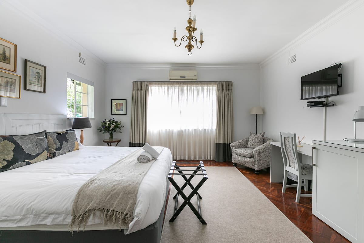 A bedroom with a bed, a desk, a chair, a TV, and a chandelier.