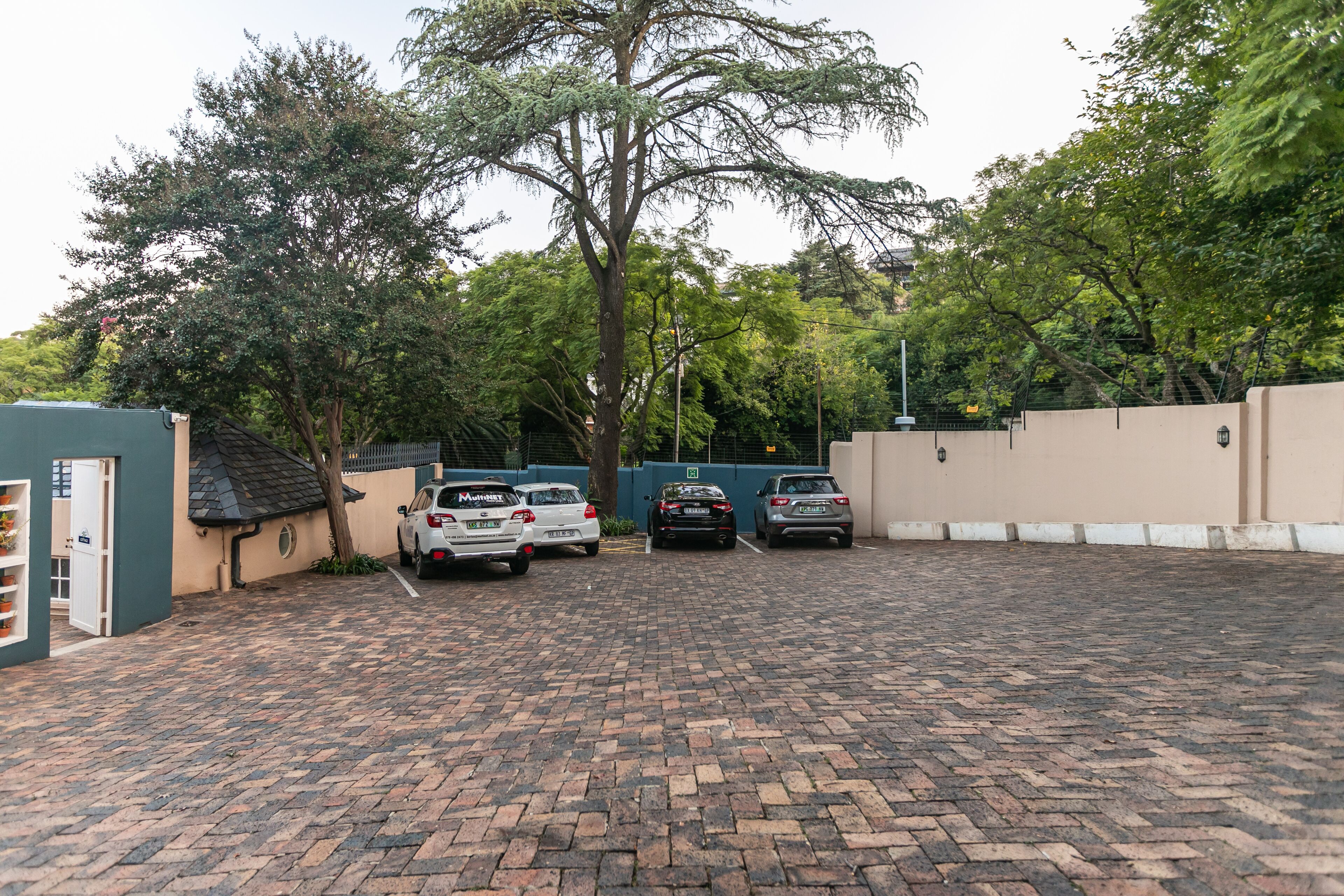 A parking area with brick pavement, a tree, and a building with a green door.