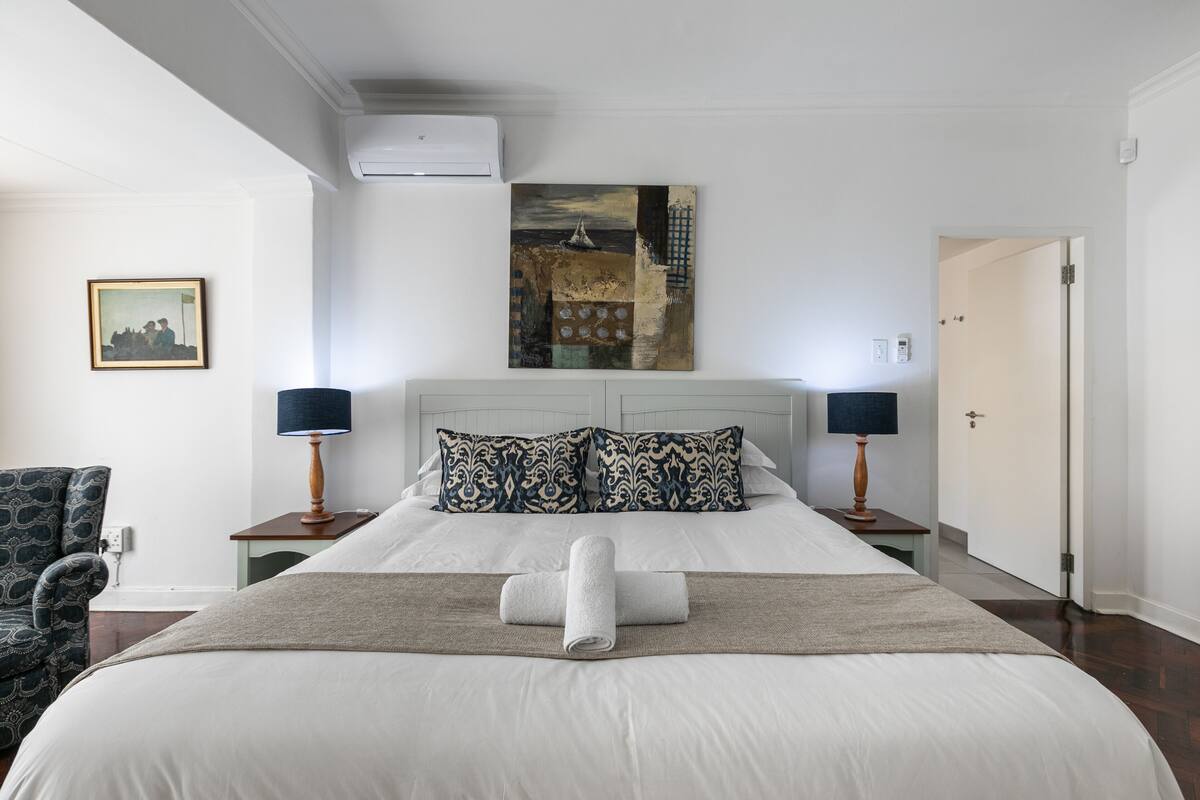 A hotel room with a large bed, two bedside tables with lamps, a painting on the wall, and a chair.
