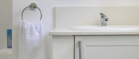 Un baño con un lavamanos blanco, un tocaderechos y un espejo sobre el lavamanos.