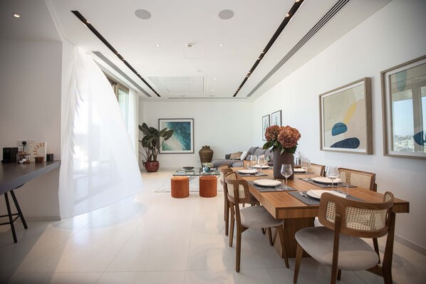 A modern dining area with a long table, chairs, and a vase of flowers. - Saffron Suite | Retreat with Skyline Views & Pool (Nicosia)