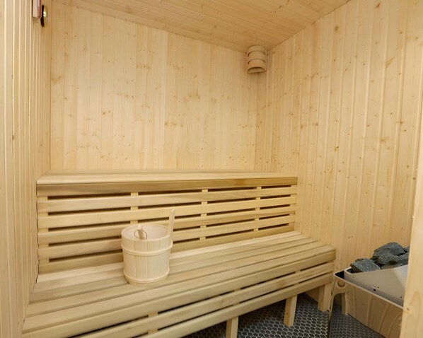 A wooden sauna bench with a bucket, a small bench, and a sauna room with a wooden ceiling and walls.