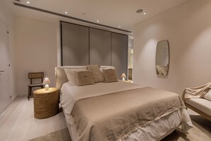 A modern bedroom with a large bed, a bedside table with a lamp, a chair, and a mirror on the wall. - Saffron Suite | Retreat with Skyline Views & Pool (Nicosia)