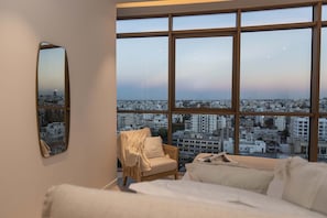 A bedroom with a large window, a bed, a chair, and a mirror. - Saffron Suite | Retreat with Skyline Views & Pool (Nicosia)