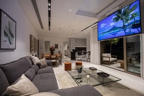 A modern living room with a grey sofa, a coffee table, and a flat-screen TV displaying a tropical scene.