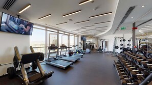 A modern gym with treadmills, weight machines, and a large TV screen.