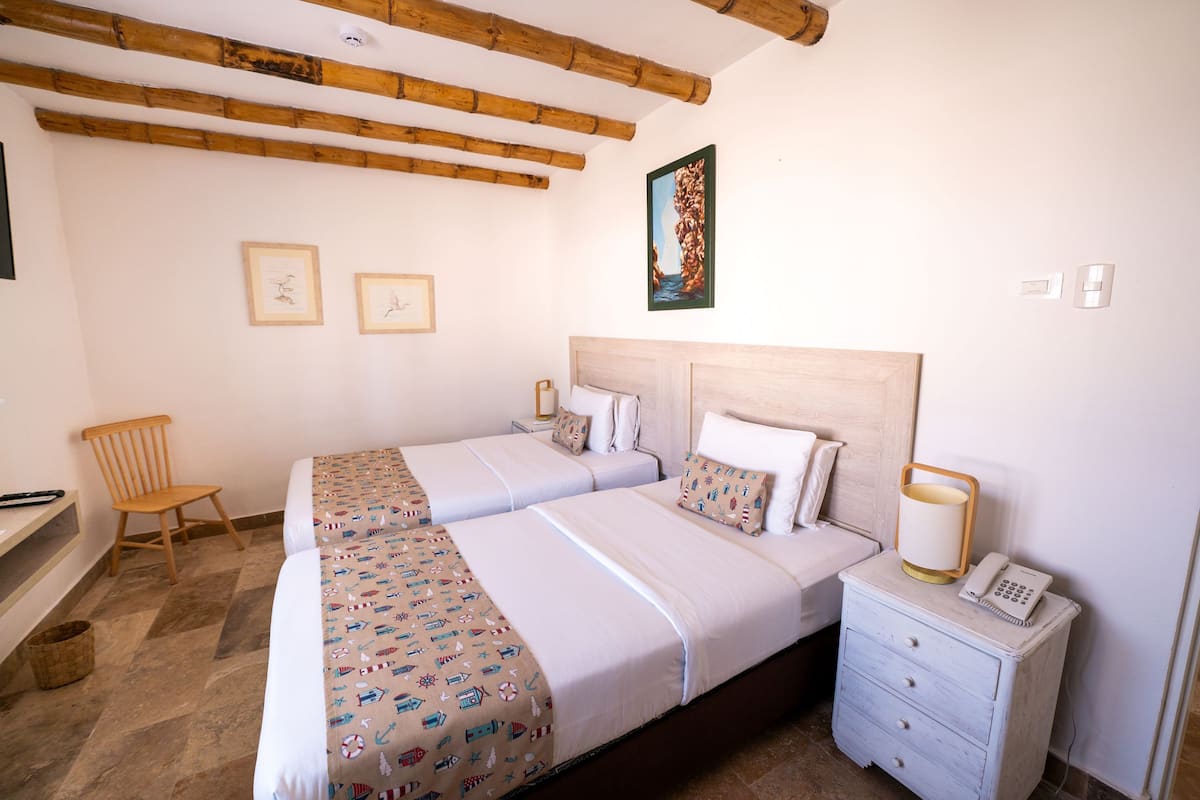 A hotel room with two beds, a wooden chair, a nightstand with a lamp, and artwork on the walls.